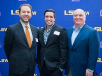 A male student and two men pose for a photo with the LSU Law logo in the background