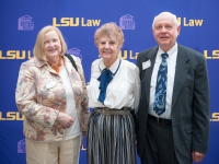 Three people pose for a photo with the LSU Law logo in the background