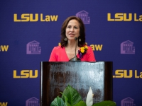 A woman wearing a red dress talks at a podium with the LSU Law logo in the background