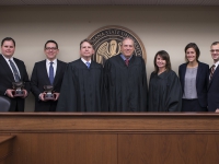 Four students wearing suits pose with three judges next to the LSU Law Center seal