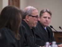 A man in judges robes speaks with a judge in the foreground and another in the background