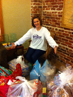 A female wearing an LSU Law PILS sweatshirt shows off wrapped presents with a brick wall in the background