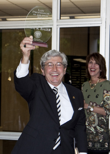 A man in a suit and tie smiles and holds up an award