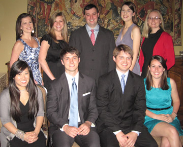 Nine students in formal attire pose for a photo with artwork in the background