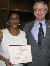 A woman holds a certificate next to a man as they smile for a photo