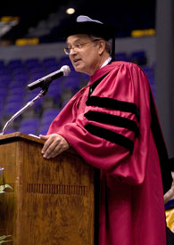 A man in a red robe speaks at a podium during the LSU Law Center Commencement