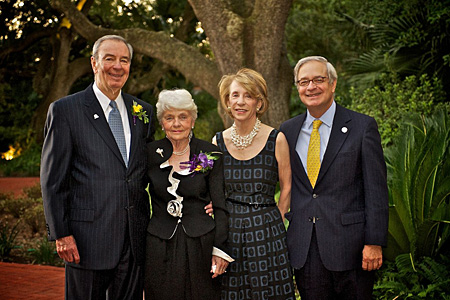 Two men and two women wearing formal attire pose for a photo with an oak tree in the background