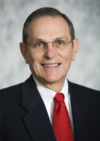 Headshot photo of man in suit with red tie and glasses