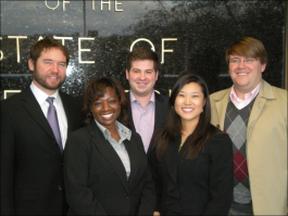 3 men and 2 women in suits pose for a photo with a black marble wall in the background