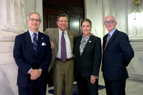 Three men and a woman pose together for a photo with marble pillars in the background