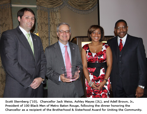 Three men and a woman pose for a photo with one man holding a glass award