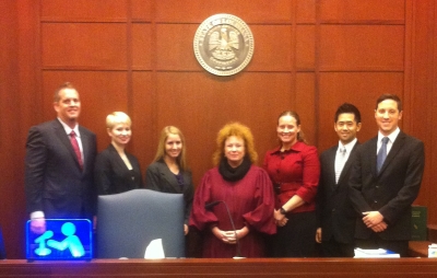 Seven people in suits stand together for a photo with the state seal of Louisiana in the background