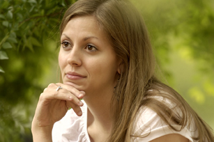 A woman poses with her head on her hand and bushes in the background