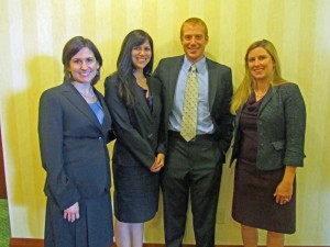 Three female and one male student wearing suits pose for a photo