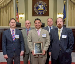 Five men in suits pose for a photo with the man in the center holding a plaque and the Louisiana Supreme Court seal in the background