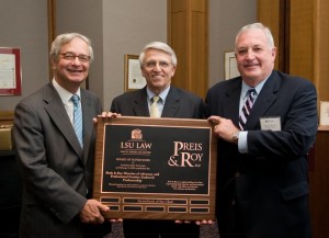 Three men wearing suits smile and hold a large wooden plaque