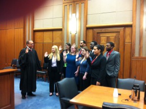 Students raise their right hands as they are sworn in by a man wearing a judge's robe