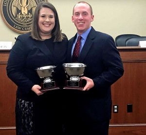 A female and male student each hold silver trophies with the LSU Law Center seal in the background