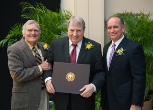 Three men wearing suits and ties pose for a photo with the man in the center holding an award