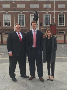 Two men and a woman wearing suits pose for a photo with a statue in the background