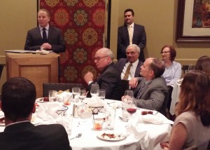 A man talks at a podium while others listen while seated at a table