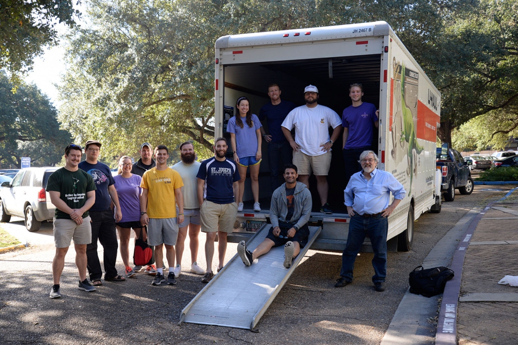A group of students and faculty pose next to and on a moving truck outside the LSU Law Center