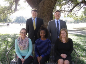 Three women and two men pose for a photo with an oak tree in the background