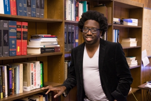 A man wearing a white shirt and black jacket stands next to a shelf with books