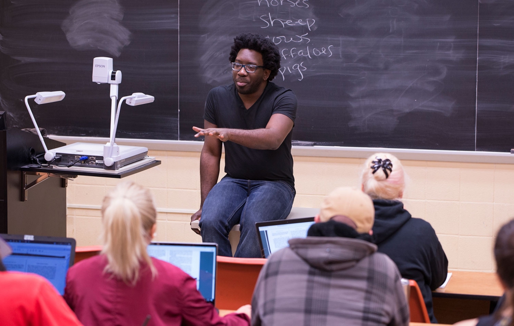 A man in a black shirt teaches in a classroom with students in the foreground