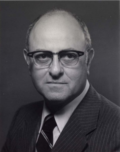 A black and white headshot photo of a man wearing a suit and tie