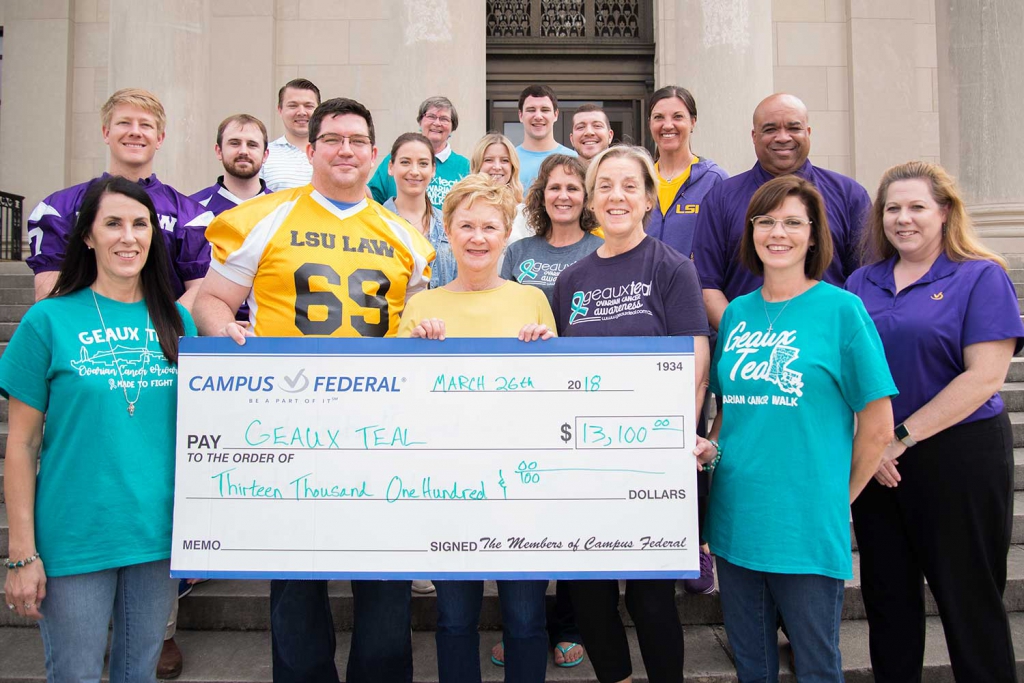 A group of people stand on the front steps of the LSU Law Center and hold a large check for $13,100