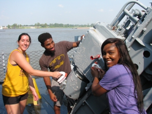 Three students clean part of a warship