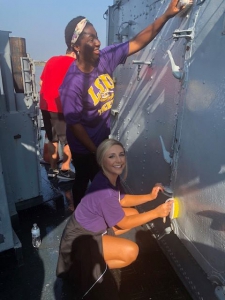 Two students clean part of a warship