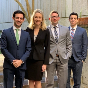 Three men and a woman pose in suits for a photo