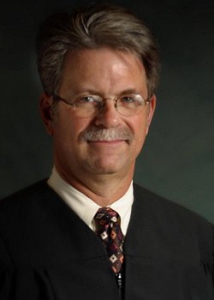 A headshot photo of a man wearing a judge's robe and tie