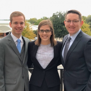 Two men and a woman in suits pose for a photo