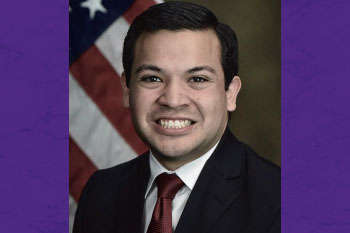 headshot of man with American flag in background