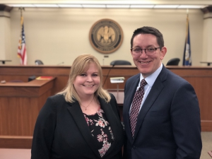 A female and male student wearing suits smile for a photo with the LSU Law courtroom in the background