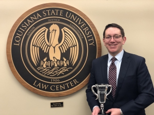 A male student holds a crystal trophy while standing next to the LSU Law Center seal